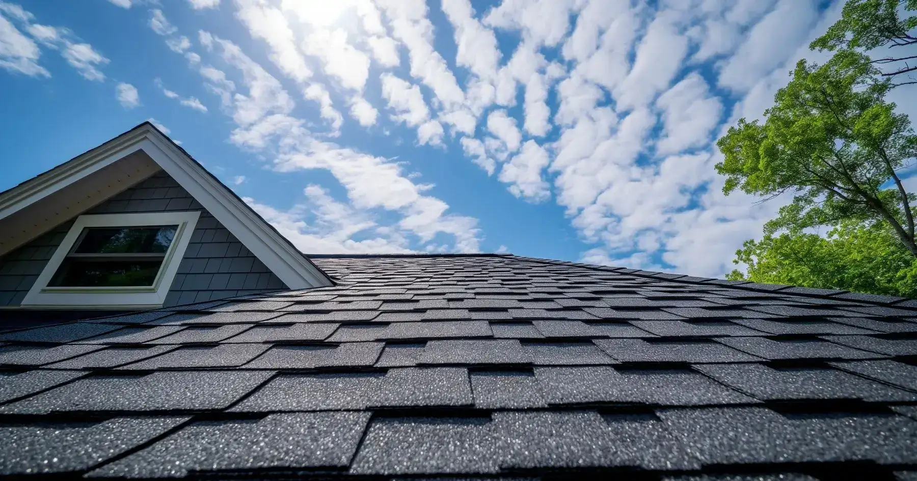Asphalt shingle roof with attic window under blue sky